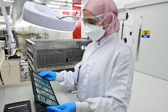 Técnica de fábrica nas instalações de montagem e teste da Intel em Penang, inspecionando uma bandeja de processadores Intel Core Ultra.