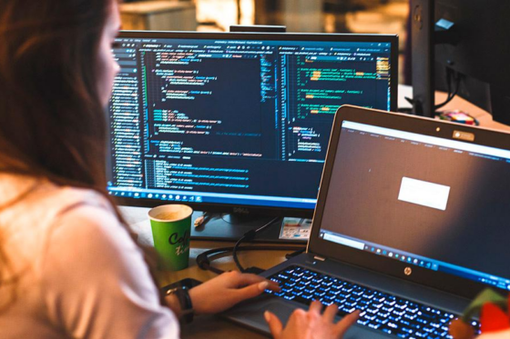 Pessoa programando em computadores com código na tela.
